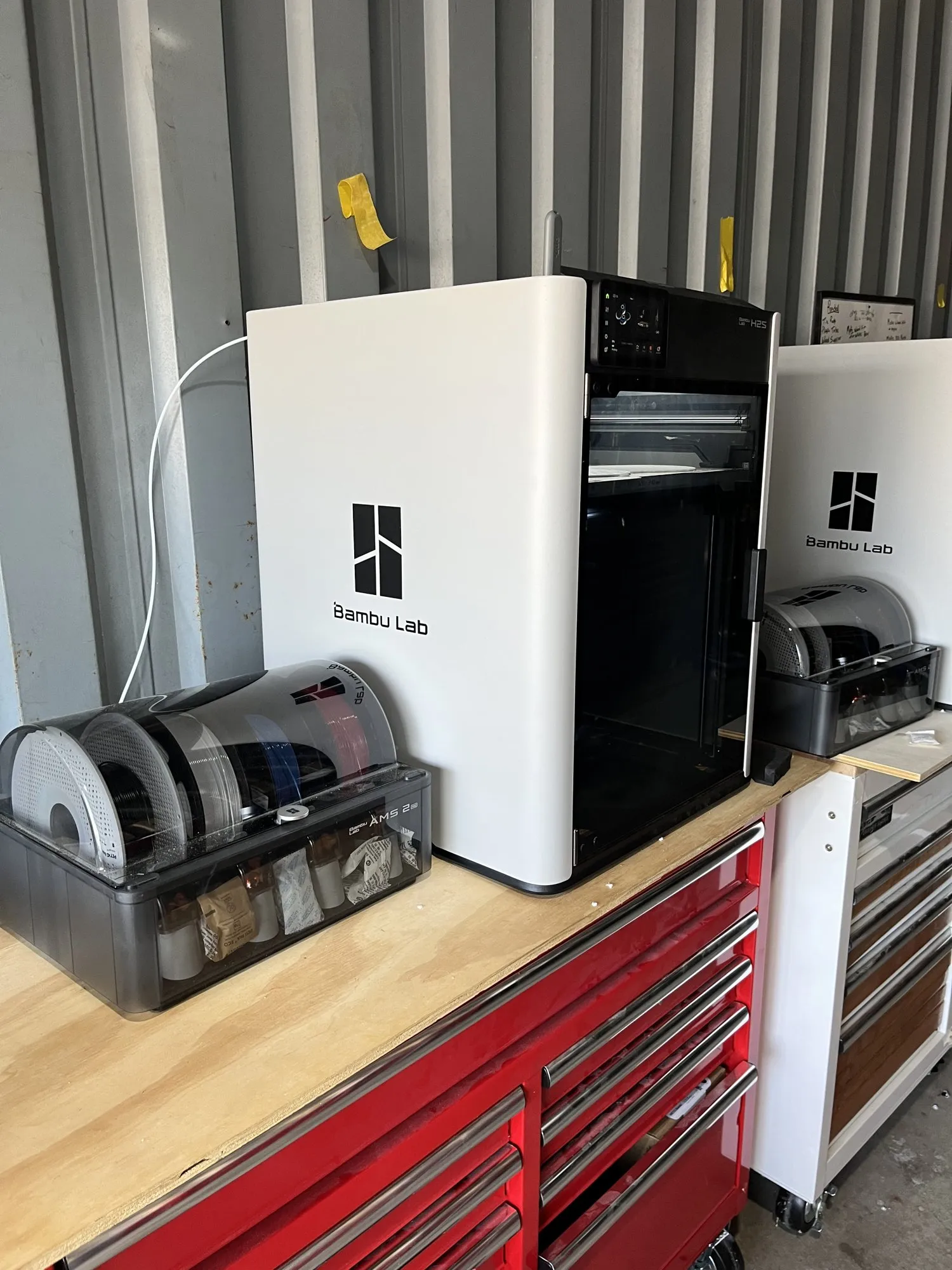 Bambu Lab H2S 3D printer on a red tool chest with an AMS 2 filament unit beside it, and a second H2S next to it