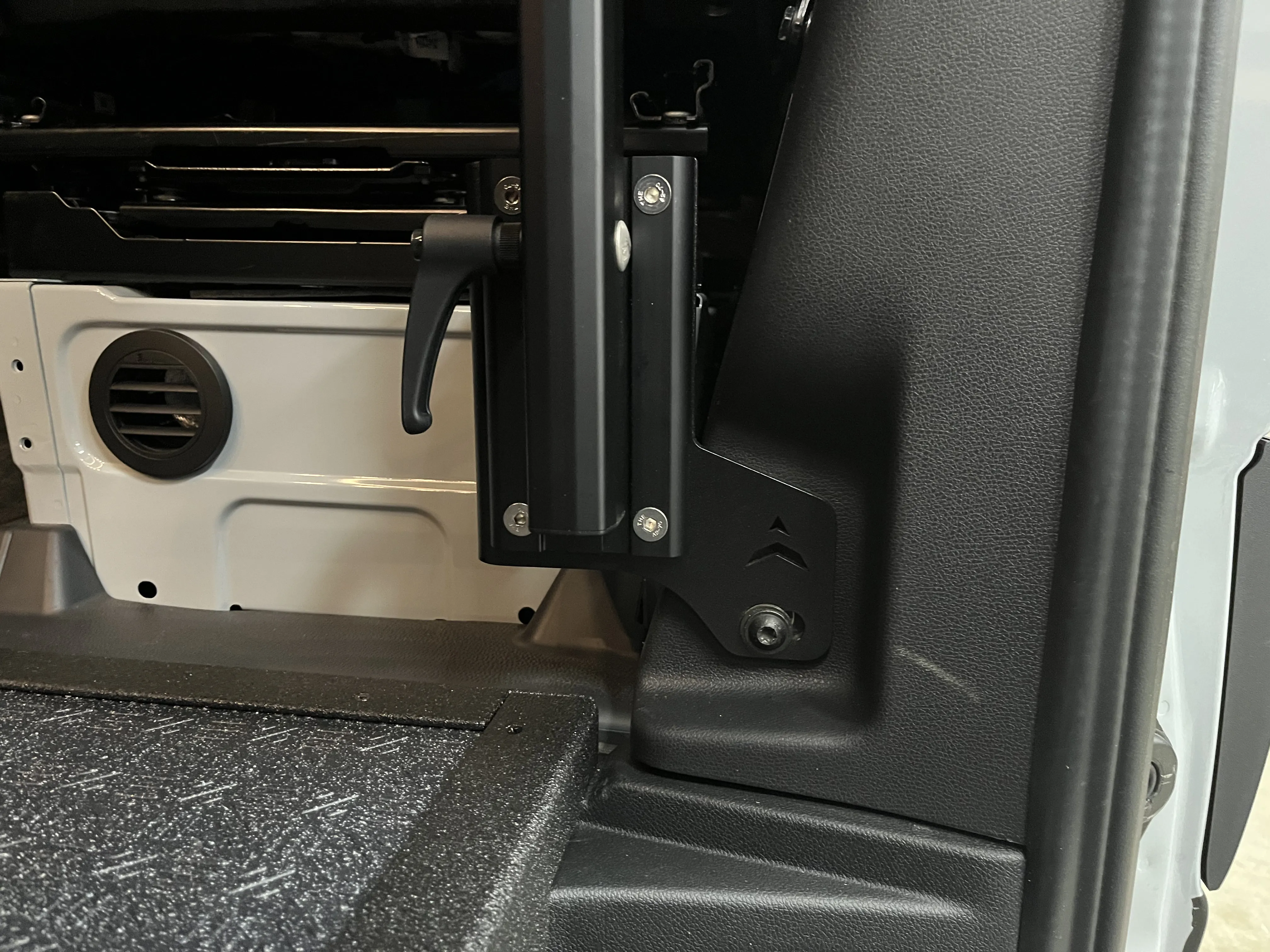 Black powder-coated Lagun table mounting bracket installed beside the seat base in an overland van