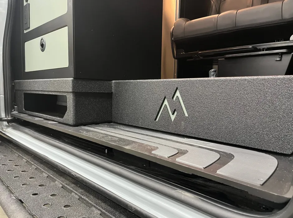 Fabricated storage cubby with Moxie Van Co logo installed at the sliding door step of a Sprinter van