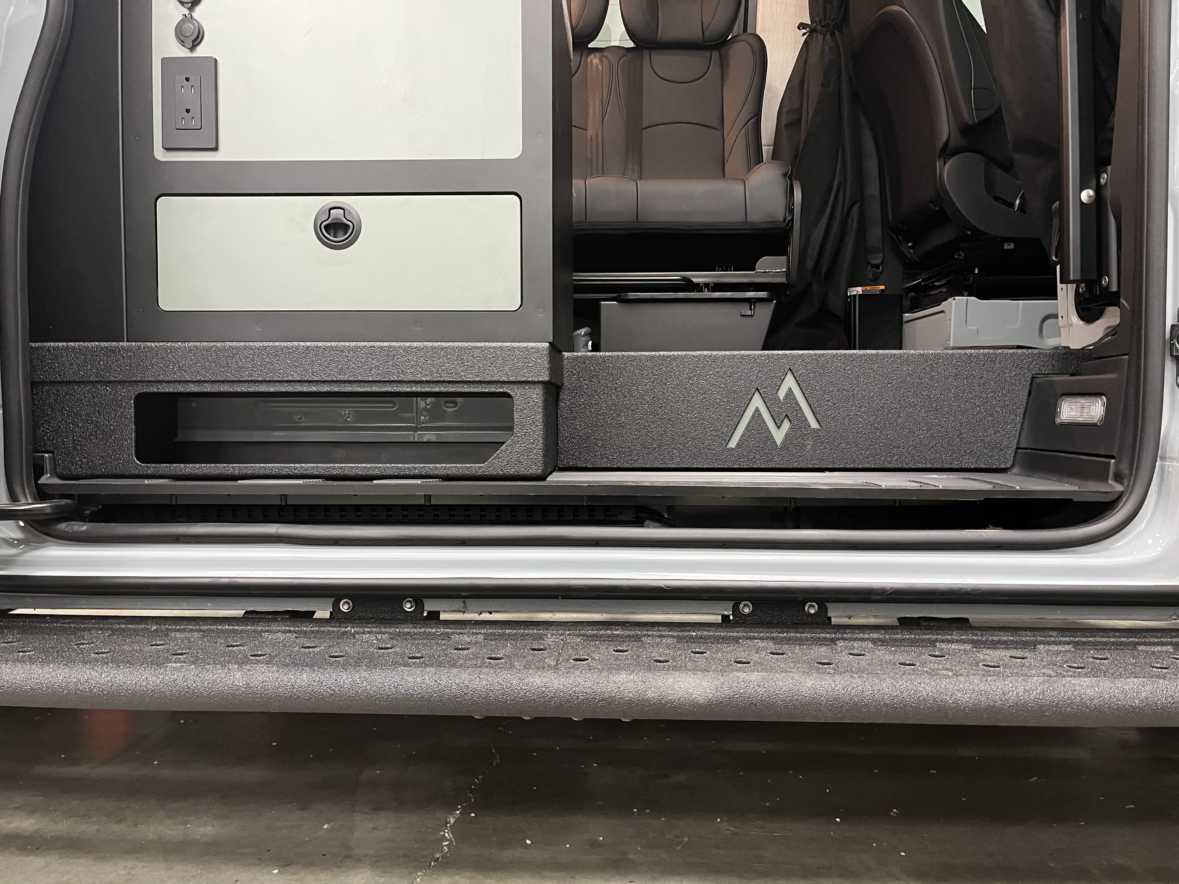 Fabricated storage cubby with Moxie Van Co logo installed at the sliding door step of a Sprinter van