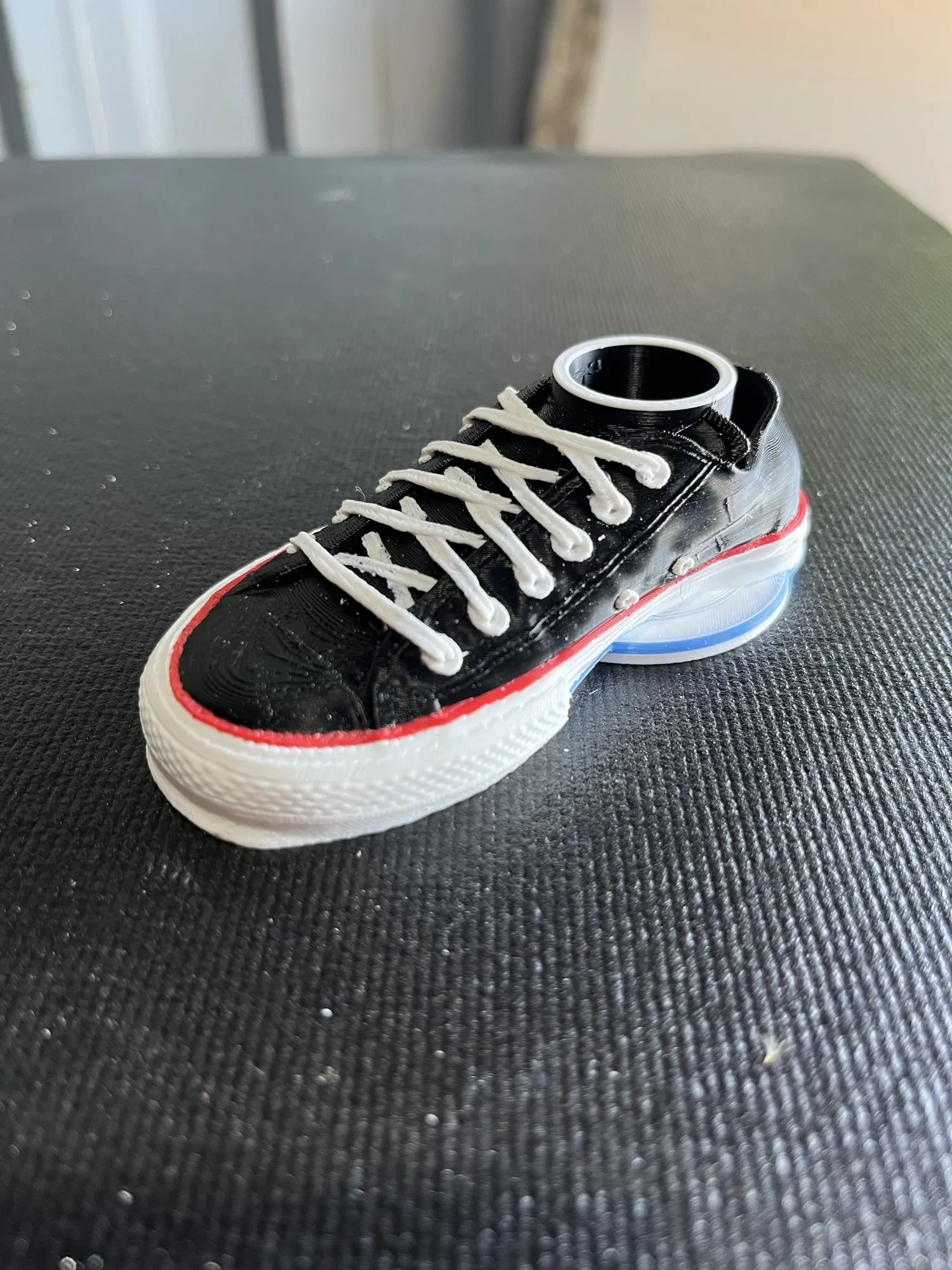 A finished 3D-printed black sneaker with white laces, a white sole, and red and blue trim